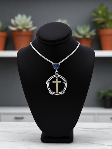 Necklace with a circular pendant featuring a cross and blue gemstone on a black bust, with a blurred indoor setting in the background.